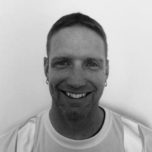 A man smiling for the camera in front of a white wall.