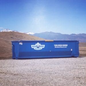 A blue dumpster sitting in the middle of a field.