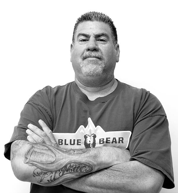 A man with tattoos and beard standing in front of a white wall.