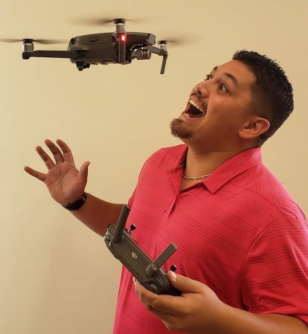 A man holding two remote controls in front of a flying camera.