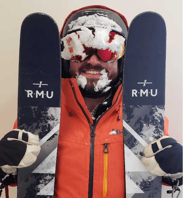 A man in an orange jacket holding two snowboards.