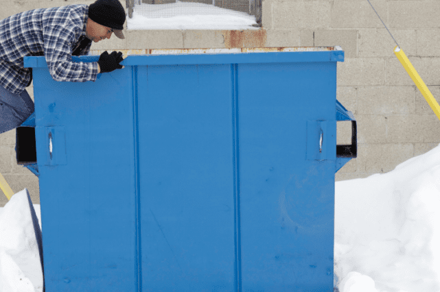 A man is leaning over the side of a dumpster.