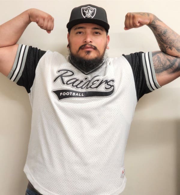 A man with tattoos and a raiders shirt.