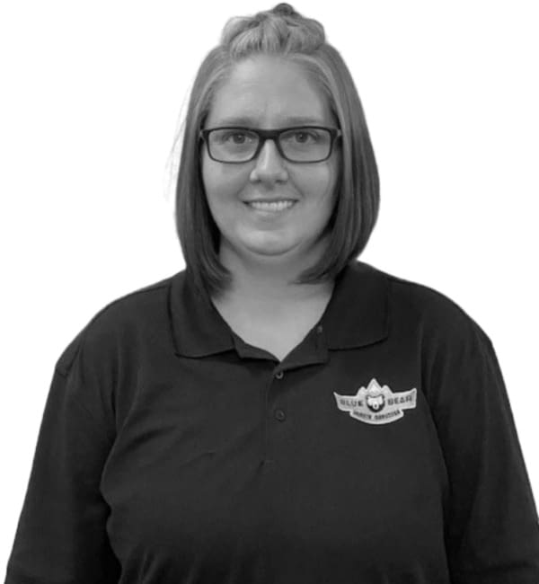 A woman in black shirt and glasses standing next to wall.