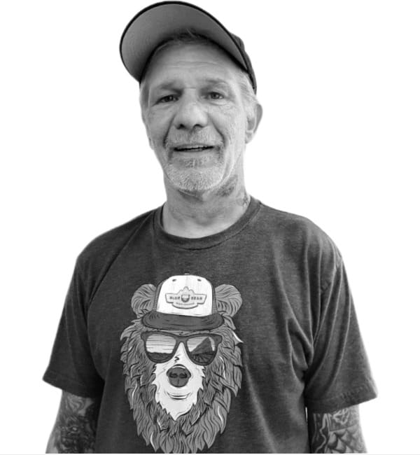 A man wearing a hat and sunglasses with a bear shirt on.