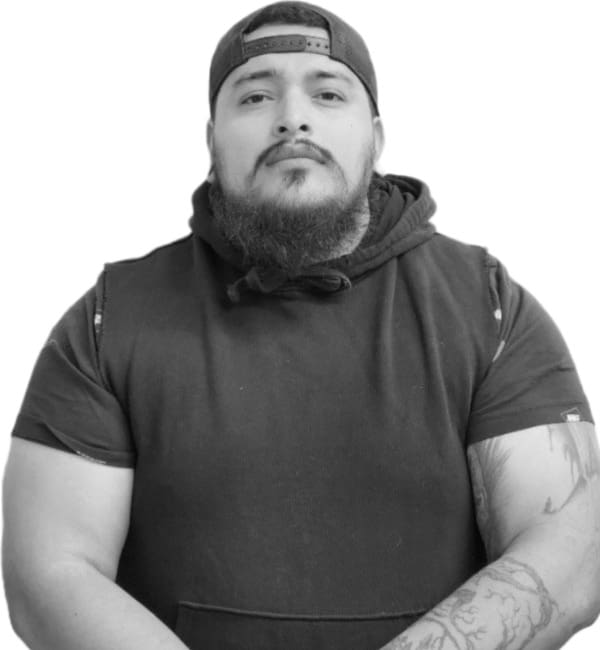 A man with beard and cap standing in front of a white wall.