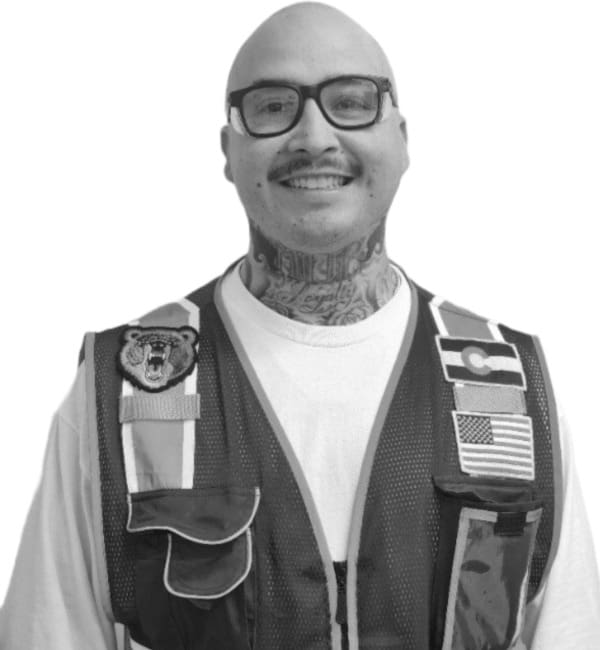 A man with tattoos and glasses wearing vest.