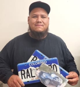 A man holding two blue license plates and a toy car.