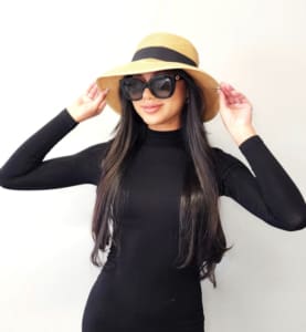 A woman in black shirt and hat holding her hair.