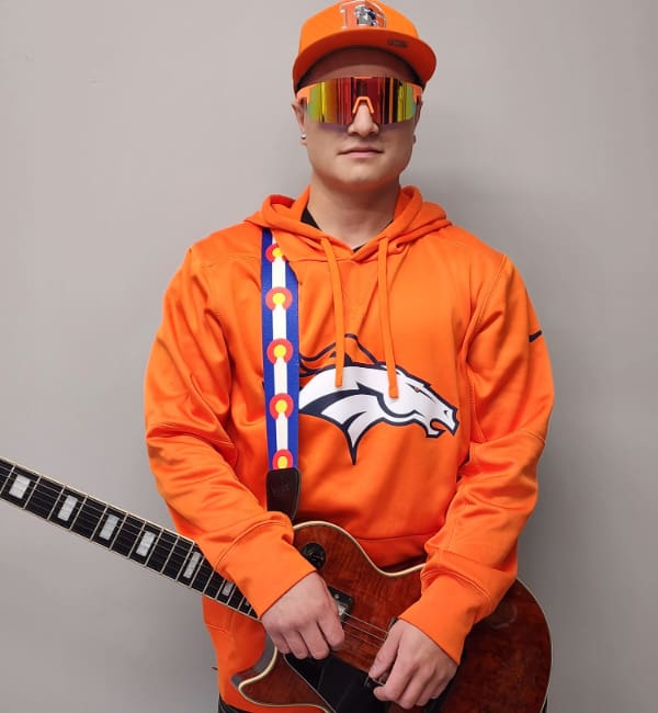 A man in an orange shirt holding a guitar.